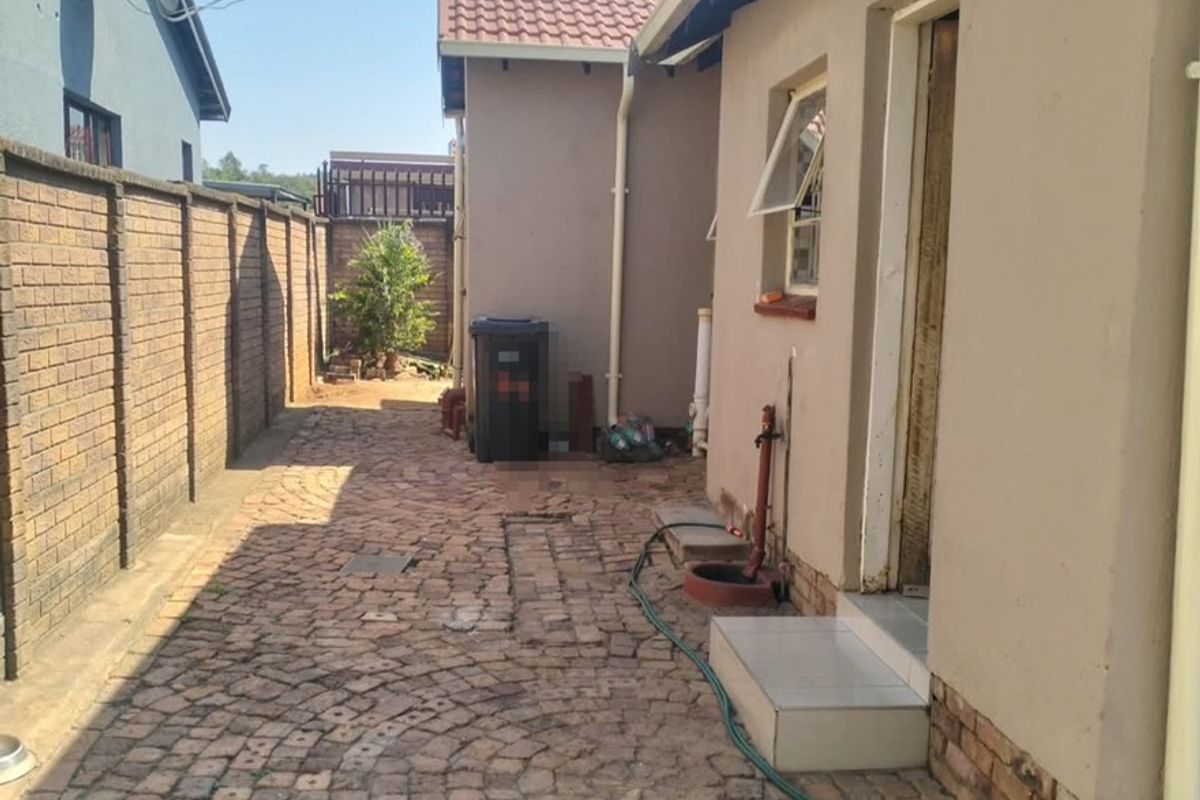A side exterior area featuring brick paving, a boundary wall, and external plumbing fixtures along the side of the house.