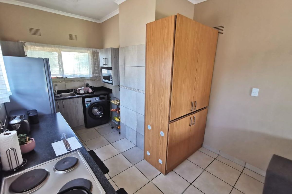Functional kitchen featuring tiled flooring, built-in cabinetry, electric hob, and a dedicated pantry unit, offering practical storage and workspace.