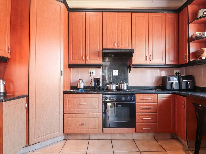 A functional kitchen featuring warm-toned wooden cabinetry, granite countertops, a built-in oven with extractor fan, and tiled flooring.
