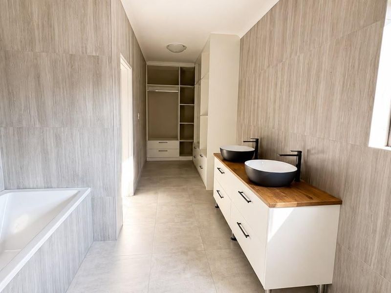Modern bathroom featuring a double vanity with vessel sinks, a freestanding bathtub, and integrated built-in wardrobe storage with neutral tiled finishes.