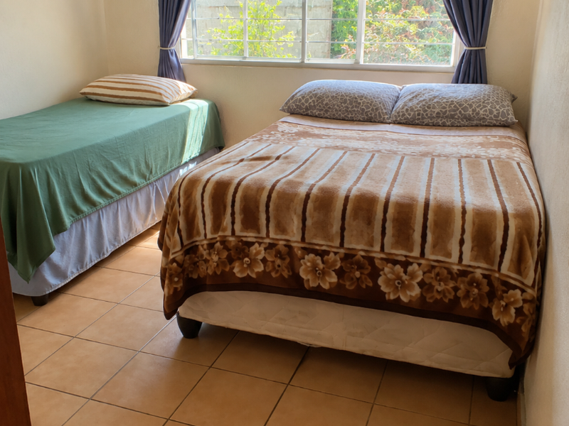 A functional bedroom featuring tiled flooring, a large sliding window with curtain rods, and a built-in floating shelf.