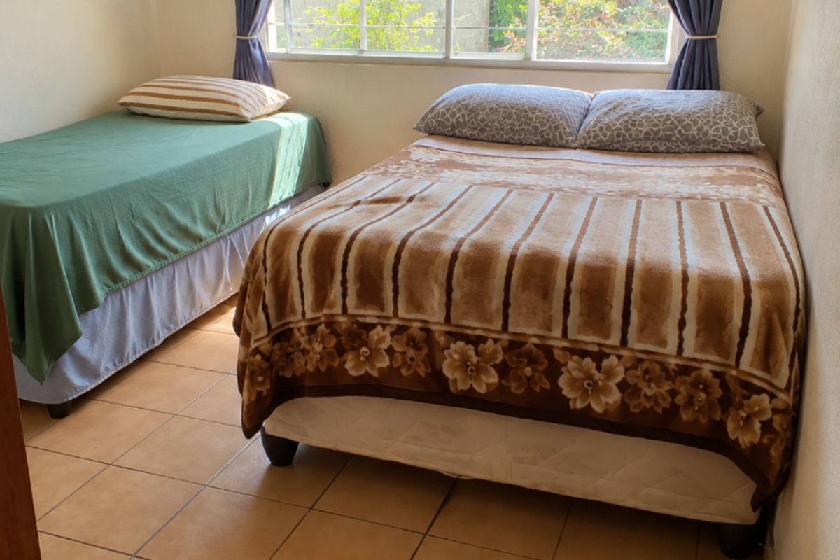 A functional bedroom featuring tiled flooring, a large sliding window with curtain rods, and a built-in floating shelf.