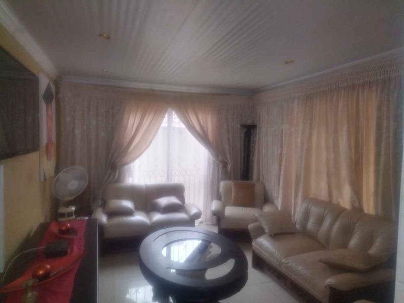 A living room featuring tiled flooring, ceiling cornices, and recessed lighting, currently furnished with a seating area.