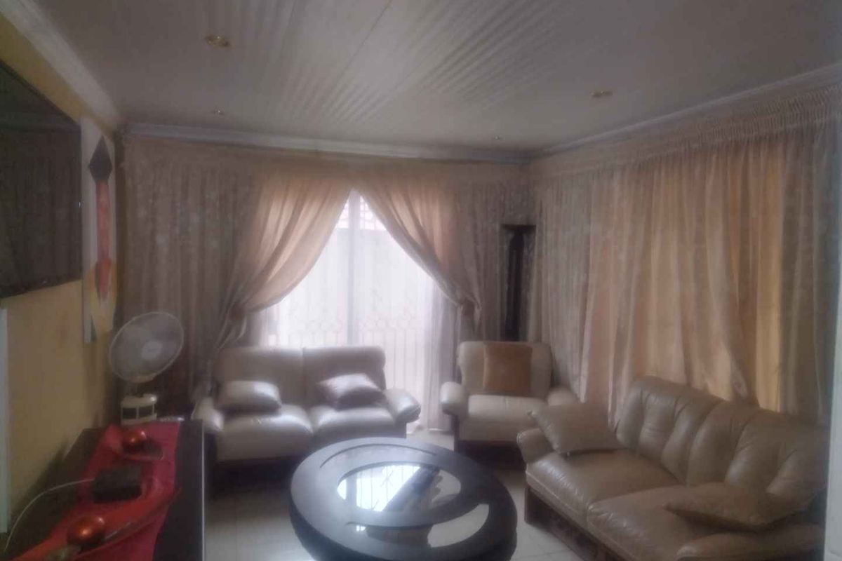 A living room featuring tiled flooring, ceiling cornices, and recessed lighting, currently furnished with a seating area.