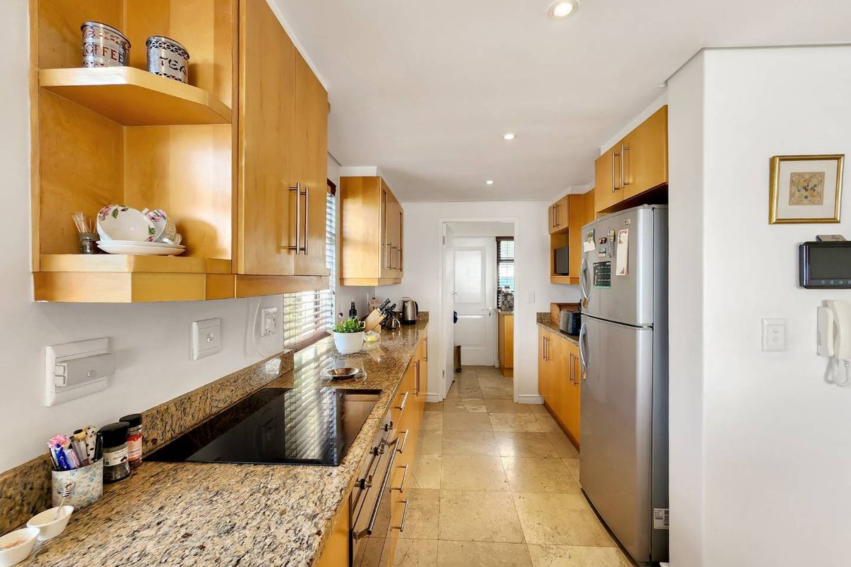 A functional galley-style kitchen featuring light wood cabinetry, granite countertops, an integrated electric hob, and tiled flooring with recessed lighting.