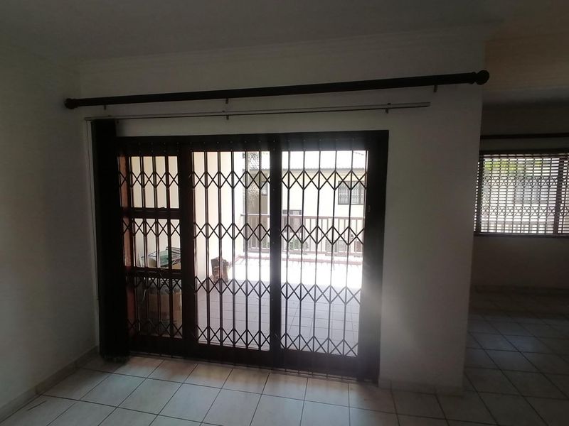 An empty living area featuring tiled flooring and sliding glass doors secured with a metal security gate, providing access to an outdoor patio.