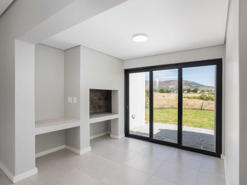 A modern, empty covered patio featuring a built-in braai, tiled flooring, and large sliding glass doors opening to a garden view.