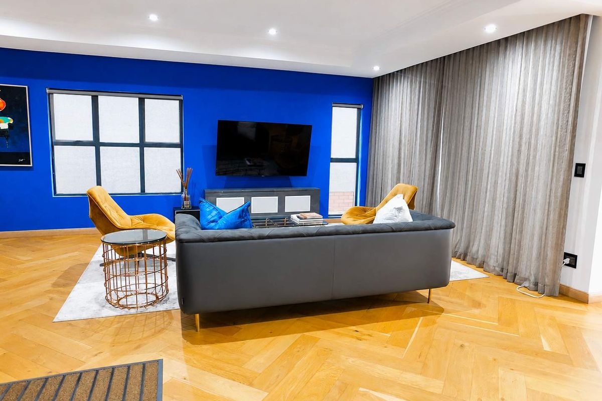 Modern living room featuring high-quality herringbone timber flooring, recessed downlighting, and a striking blue feature wall with integrated window and television placement.