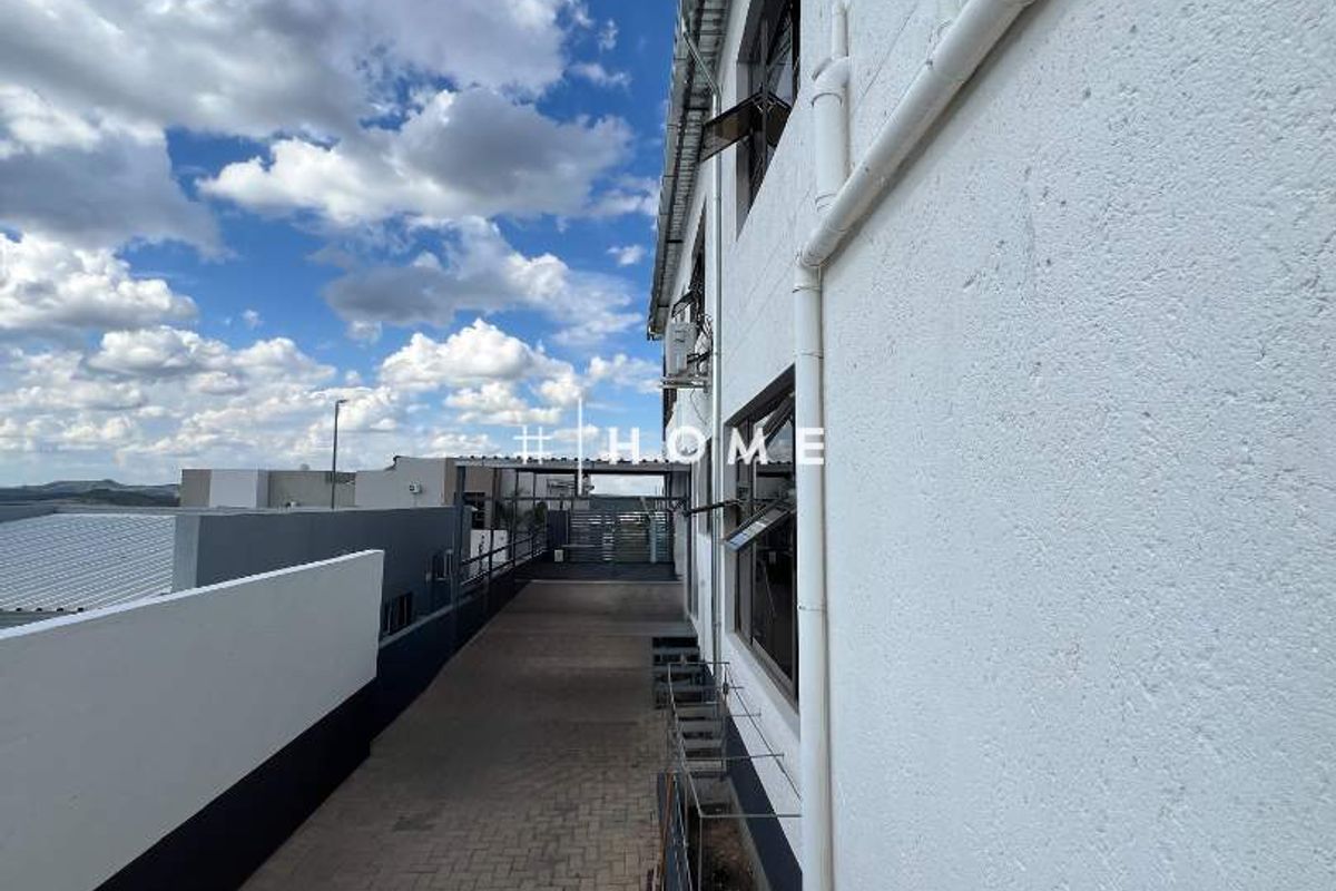 A paved side walkway along the exterior of the building featuring white rendered walls and external drainage infrastructure.