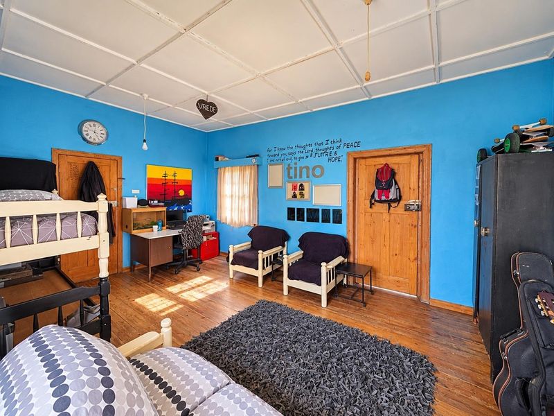 A spacious bedroom featuring timber flooring, solid wood doors, and a panelled ceiling, offering a functional layout with potential for modern updates.