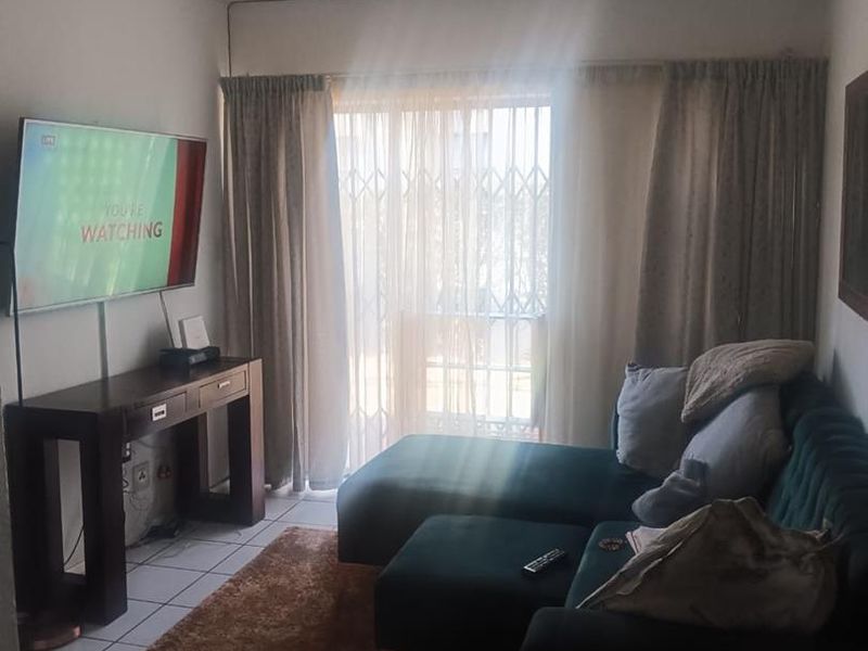 A living room featuring tiled flooring and a sliding door with a security gate, providing access to an outdoor area.