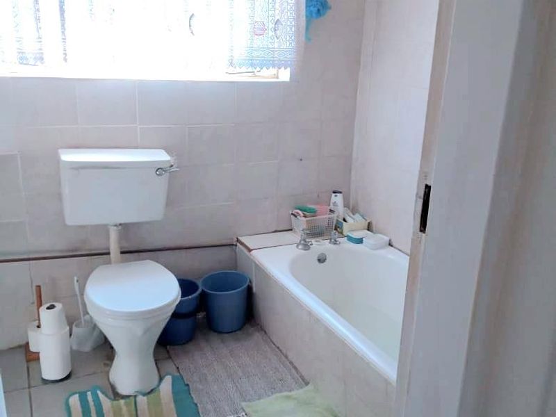 A functional bathroom featuring a standard toilet, bathtub, and tiled finishes throughout.