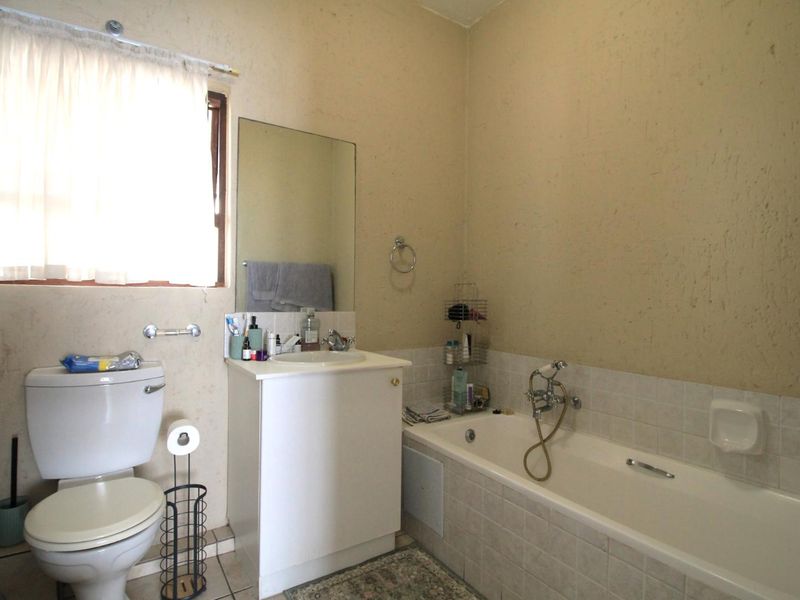 A functional bathroom featuring a standard toilet, vanity unit with basin, and a tiled bathtub with shower mixer.