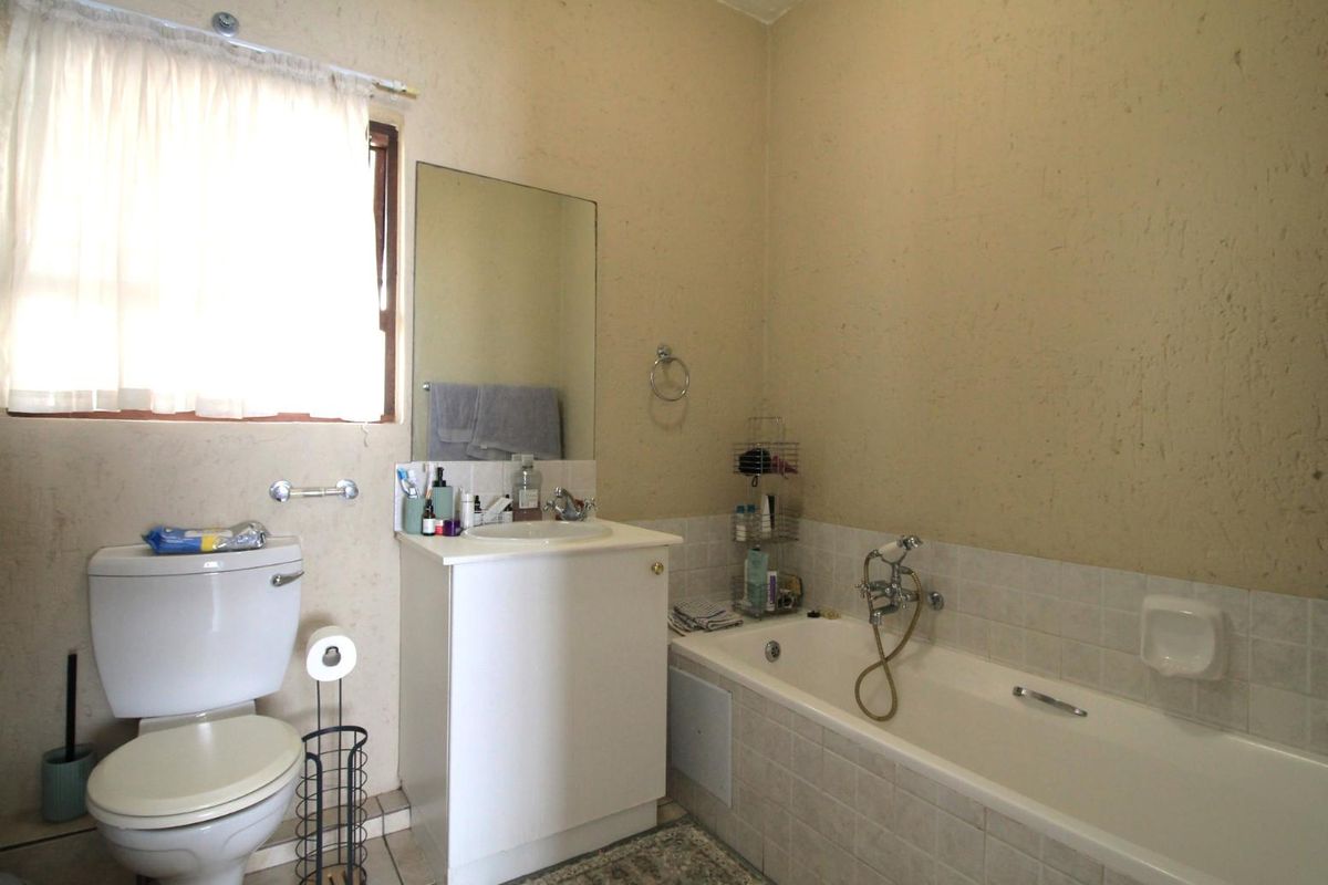 A functional bathroom featuring a standard toilet, vanity unit with basin, and a tiled bathtub with shower mixer.