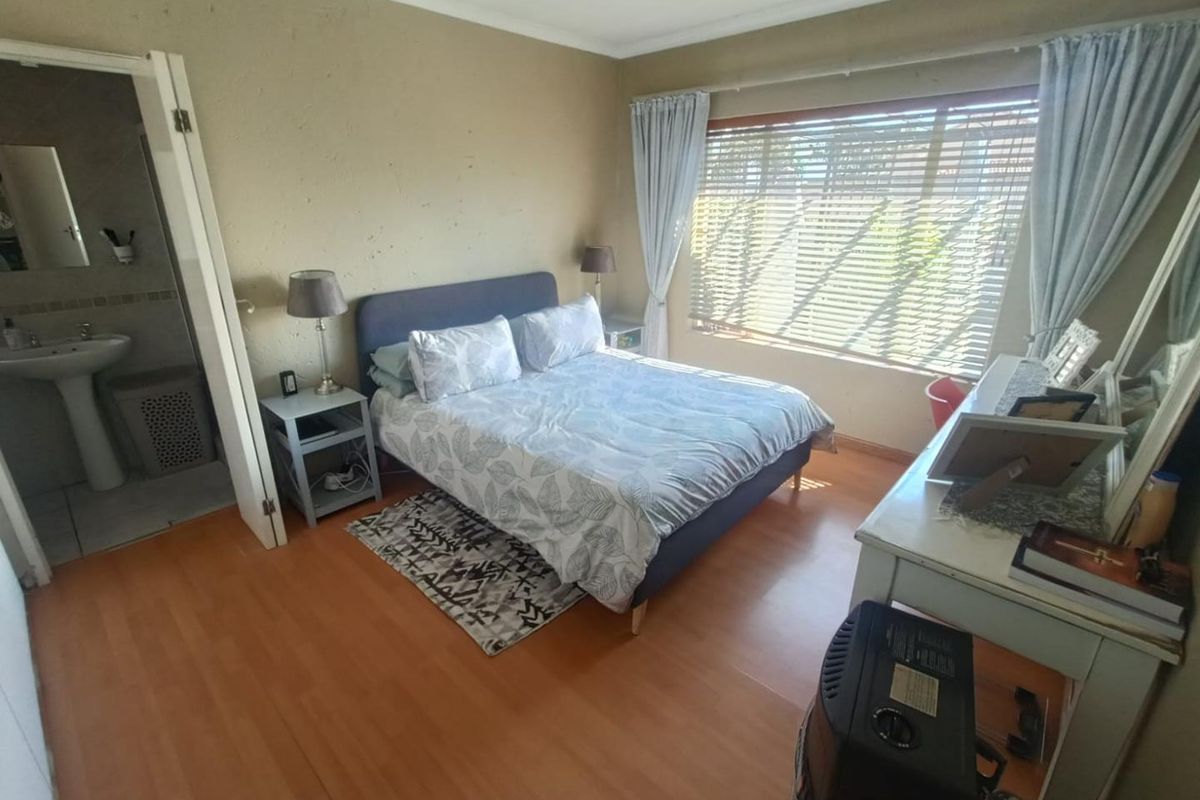 A bedroom featuring laminate flooring, recessed lighting, and an en-suite bathroom, offering a functional layout with natural light through venetian blinds.