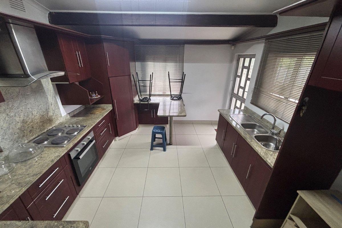A functional kitchen featuring dark wood cabinetry, granite countertops, a built-in oven, hob, extractor fan, and a double stainless steel sink.
