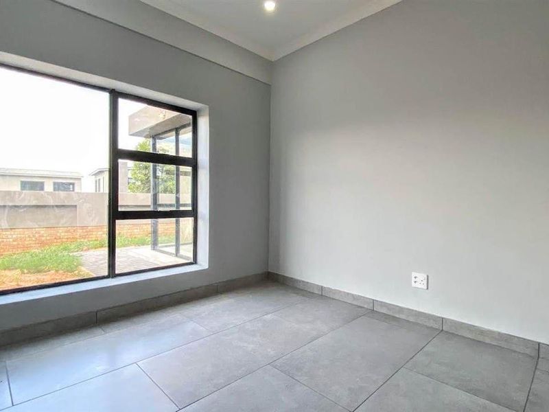 A bright, modern, and empty bedroom featuring large aluminium-framed windows, neutral grey tiled flooring, and clean finishes, ready for personalization.