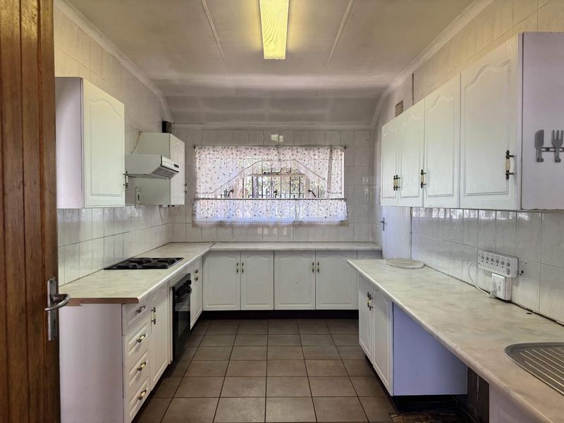 A functional, galley-style kitchen featuring white cabinetry, laminate countertops, tiled walls, and floor, equipped with a built-in oven and hob.