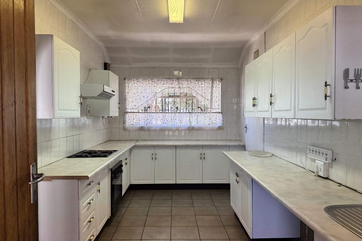 A functional, galley-style kitchen featuring white cabinetry, laminate countertops, tiled walls, and floor, equipped with a built-in oven and hob.