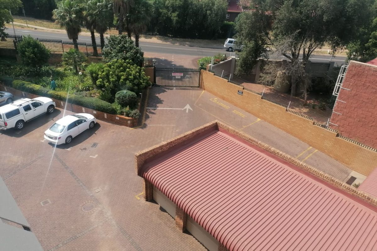 An elevated view of the apartment complex entrance, featuring paved driveway, secure gate access, and covered garage structures.