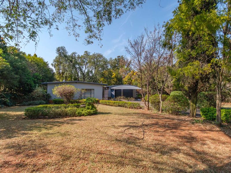A view of the front exterior of the house, featuring a spacious garden, mature trees, and a driveway leading to the garage.