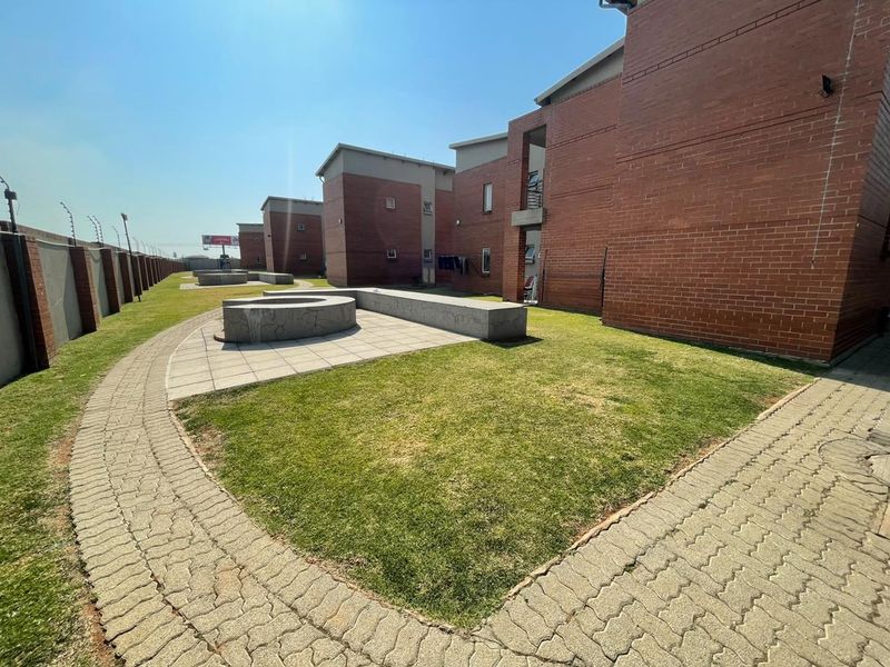 A view of the rear exterior of the apartment complex, featuring brick facades, paved walkways, and communal lawn areas with concrete seating.