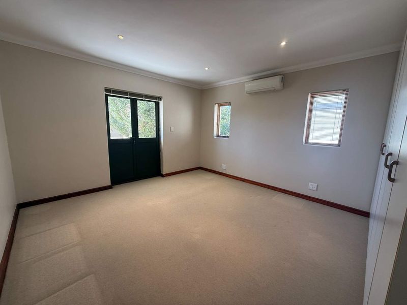 A spacious, empty bedroom featuring neutral carpeting, built-in cupboards, a split-system air conditioner, and direct access to the outdoors via double doors.