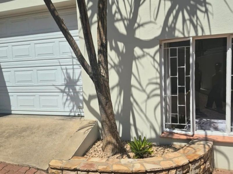 Front exterior view featuring a paved driveway, a stone-clad planter bed, a garage door, and a window with security bars.