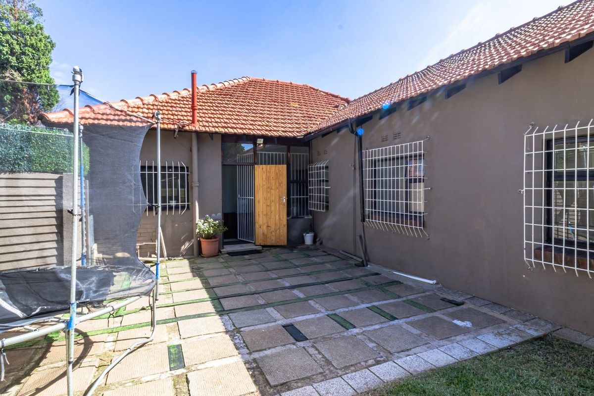 Rear exterior view of the house featuring a paved patio area, terracotta tiled roof, and security bars on windows.