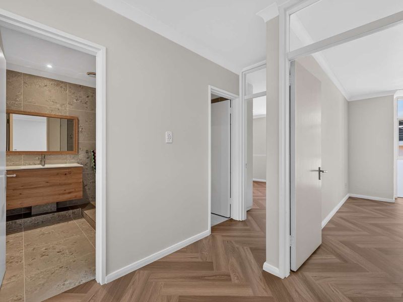 A bright, modern hallway featuring herringbone flooring, clean neutral walls, and access to a contemporary bathroom with a timber vanity and stone tiling.