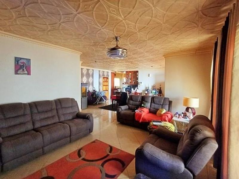 Spacious open-plan living area featuring decorative ceiling tiles, a central ceiling fan, and tiled flooring, connecting to a dining and kitchen space.