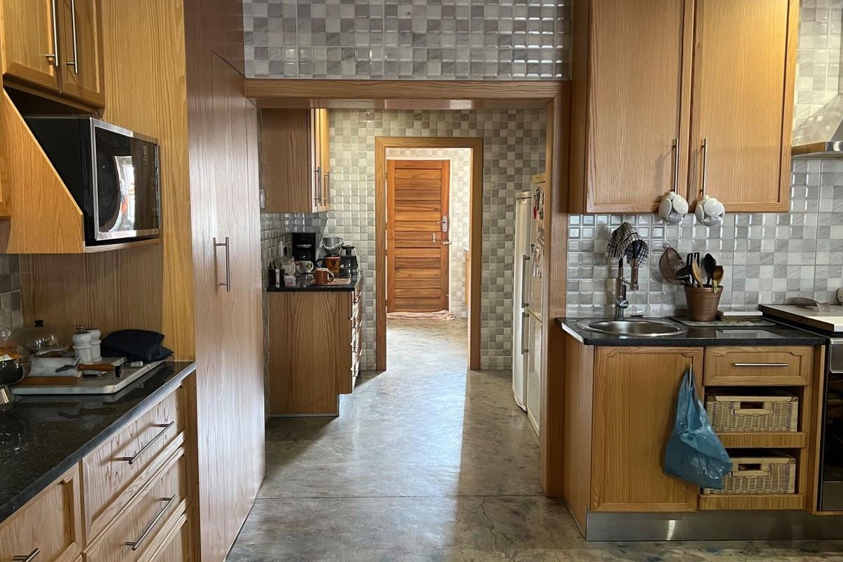A functional kitchen featuring wood-toned cabinetry, granite countertops, a stainless steel extractor fan, and a tiled backsplash, leading into a secondary prep area.