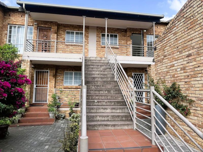 Rear exterior view of a two-story townhouse featuring a brick facade, central concrete staircase with metal railings, and a paved courtyard area.