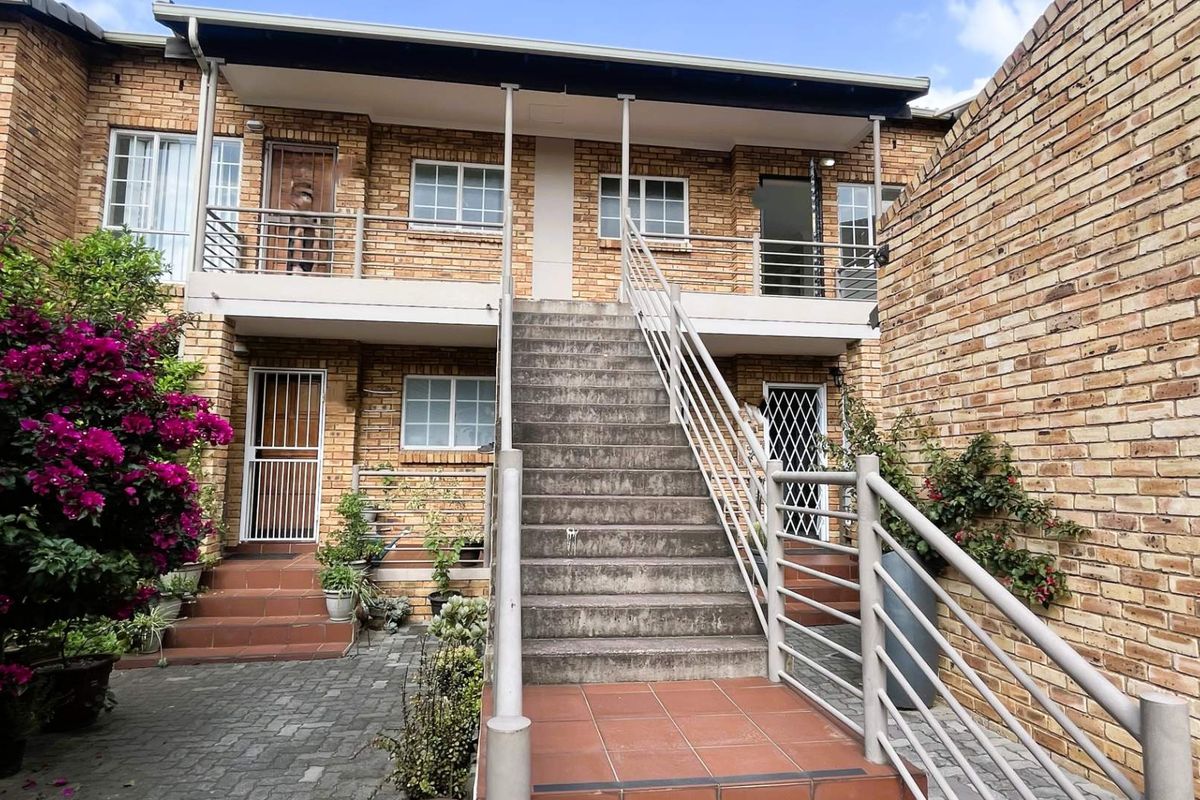 Rear exterior view of a two-story townhouse featuring a brick facade, central concrete staircase with metal railings, and a paved courtyard area.