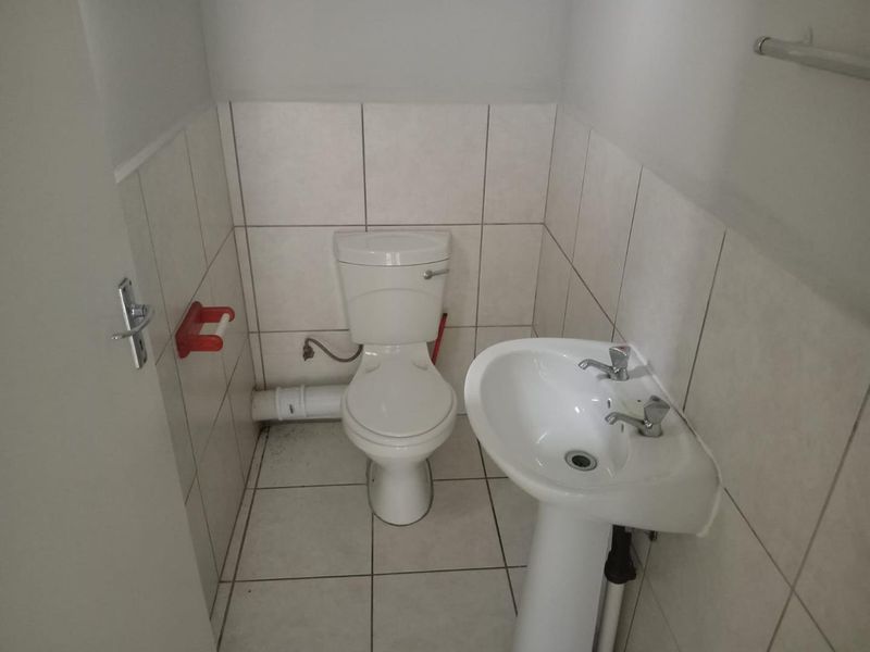 A compact office bathroom featuring a pedestal basin, toilet, and neutral ceramic tiling throughout.