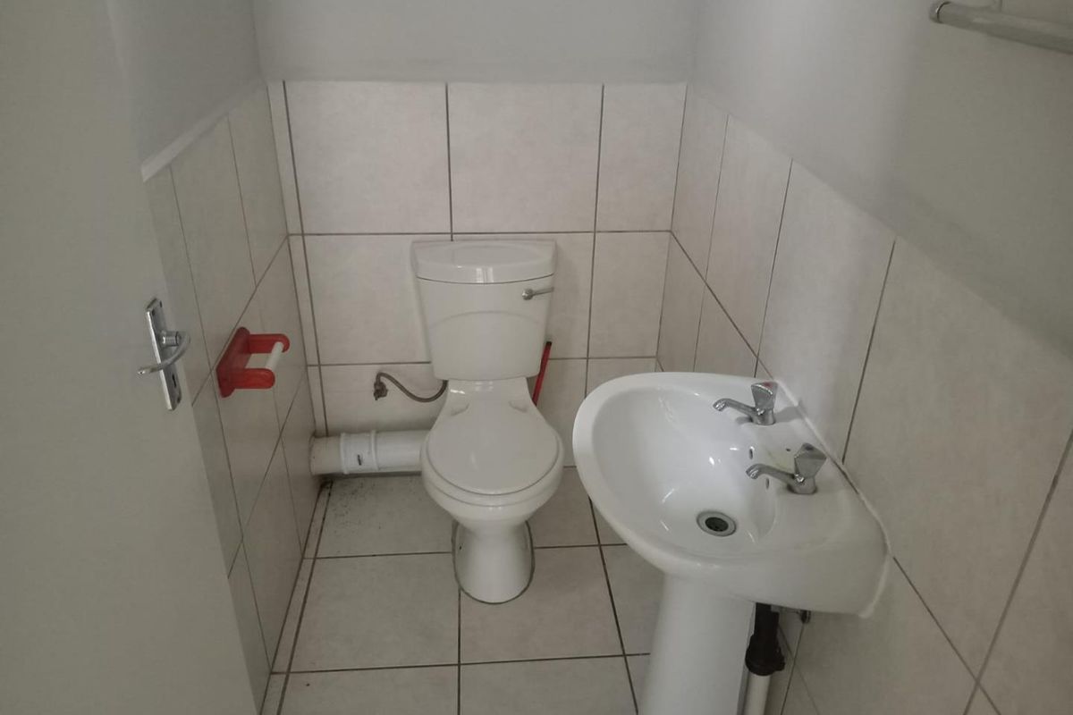 A compact office bathroom featuring a pedestal basin, toilet, and neutral ceramic tiling throughout.