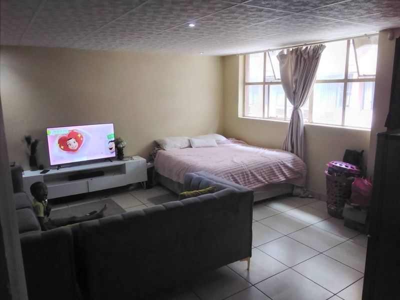 An open-plan living and sleeping area featuring tiled flooring, recessed ceiling lights, and large windows providing natural light.