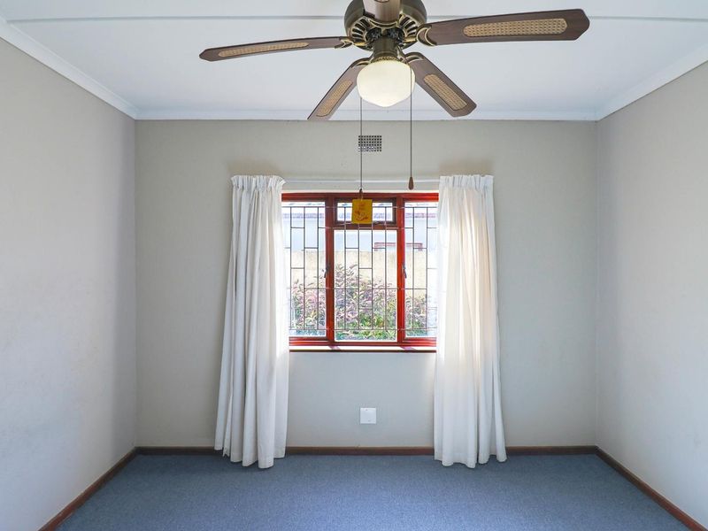 An empty bedroom featuring carpeted flooring, a ceiling fan, and a window fitted with security bars.