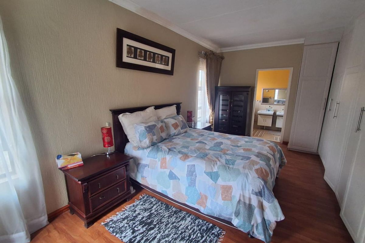 A well-maintained bedroom featuring wood-look flooring, built-in cupboards, and an en-suite bathroom access.