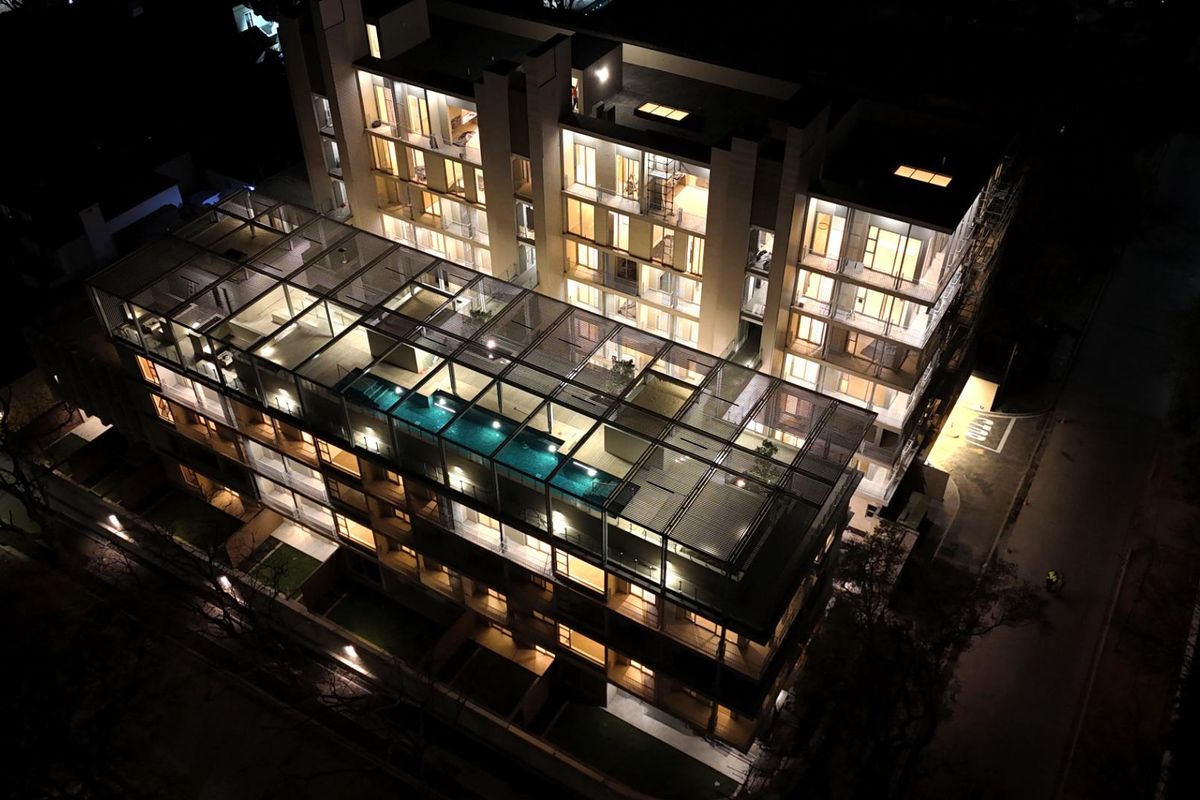 Stunning night-time aerial view of a modern multi-level apartment complex featuring a rooftop swimming pool and illuminated architectural design.