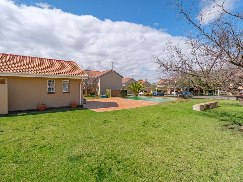 A well-maintained communal outdoor area featuring a swimming pool, paved patio space, and a large lawn area within an apartment complex.