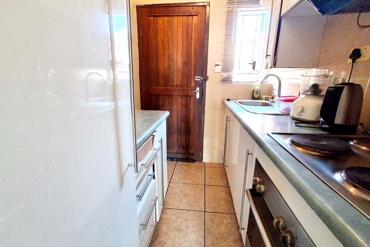 A functional galley-style kitchen featuring built-in cabinetry, laminate countertops, integrated oven and hob, and tiled flooring with a rear access door.