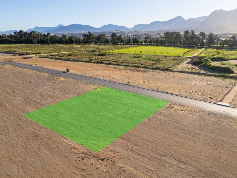 Aerial view of a vacant residential plot in a developing estate, featuring road access and scenic mountain views.