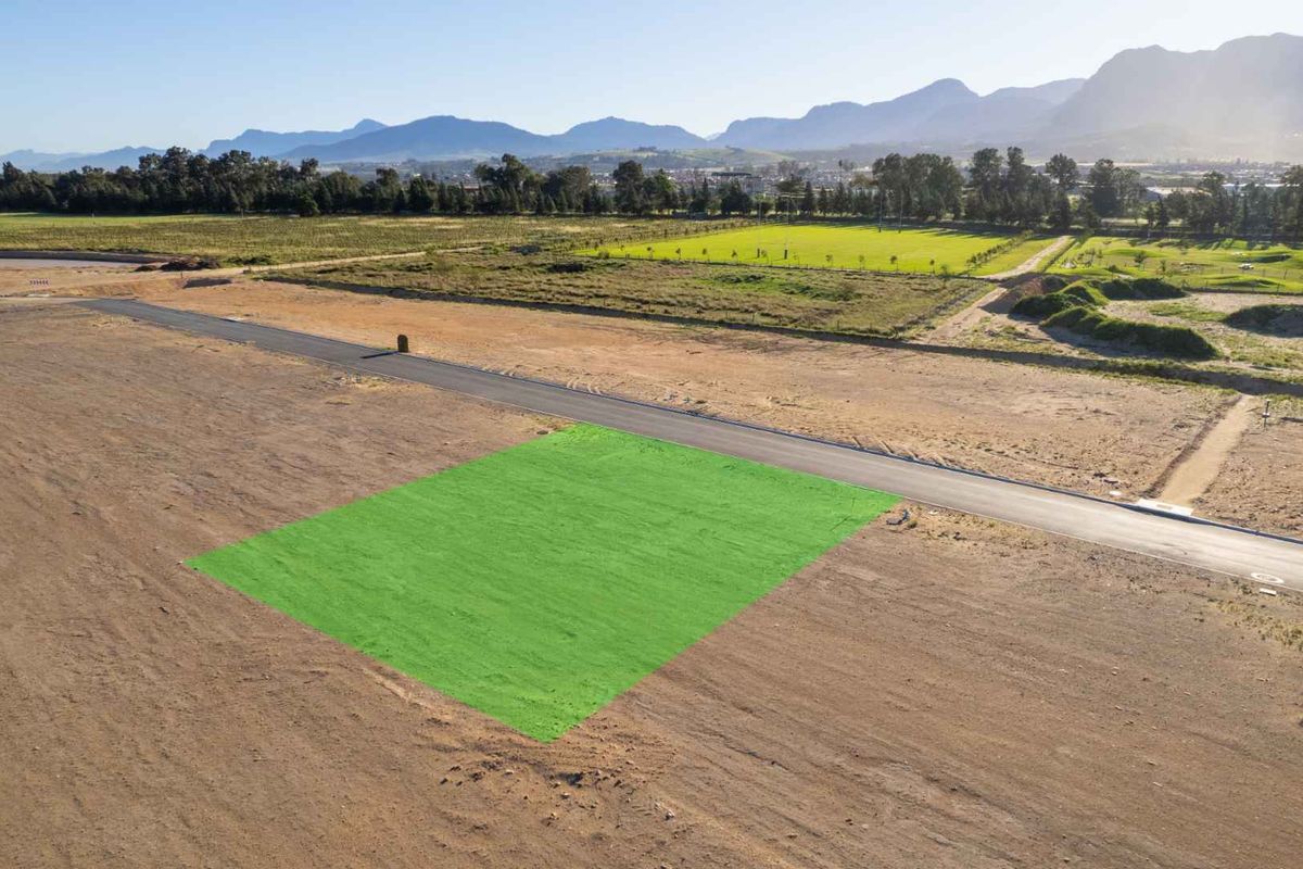 Aerial view of a vacant residential plot in a developing estate, featuring road access and scenic mountain views.