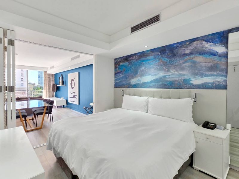 A modern bedroom featuring ducted air conditioning, recessed lighting, and a sliding glass partition connecting to an adjacent living area.