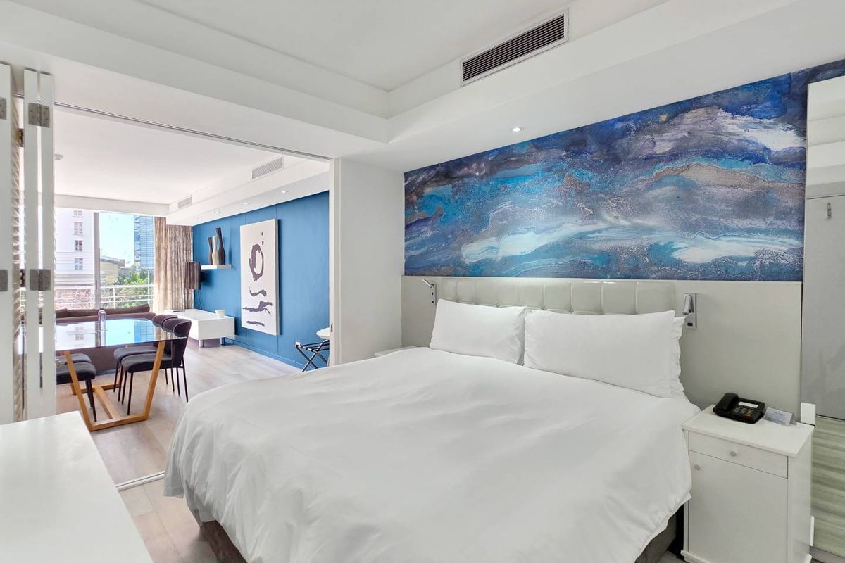 A modern bedroom featuring ducted air conditioning, recessed lighting, and a sliding glass partition connecting to an adjacent living area.
