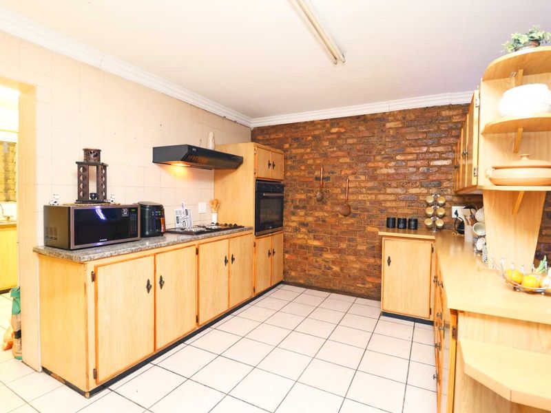 A functional kitchen featuring wooden cabinetry, granite countertops, a built-in oven, and a distinctive exposed brick feature wall with tiled flooring.