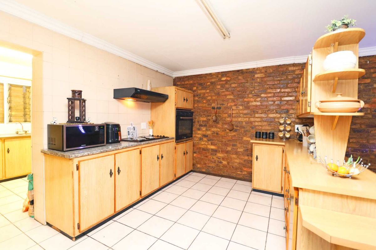 A functional kitchen featuring wooden cabinetry, granite countertops, a built-in oven, and a distinctive exposed brick feature wall with tiled flooring.