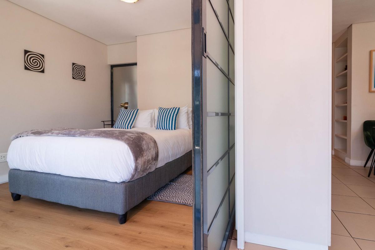 A modern bedroom featuring laminate flooring, a sliding glass partition door, and built-in shelving in the adjacent hallway area.
