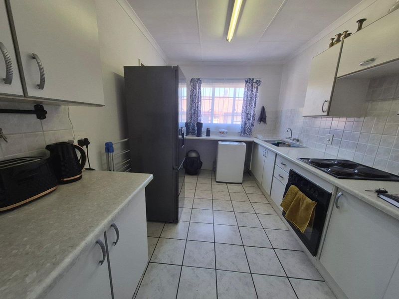 Functional galley-style kitchen featuring white cabinetry, laminate countertops, ceramic tile flooring, and integrated oven and hob.